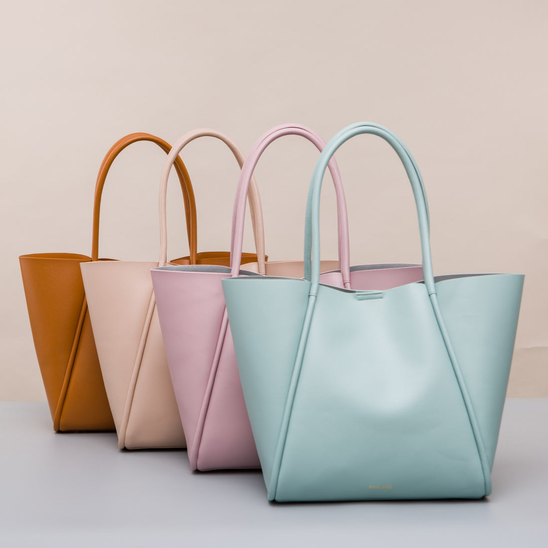 Four PU tote bags in tan, cream, pink and pale blue with twin rounded handles.