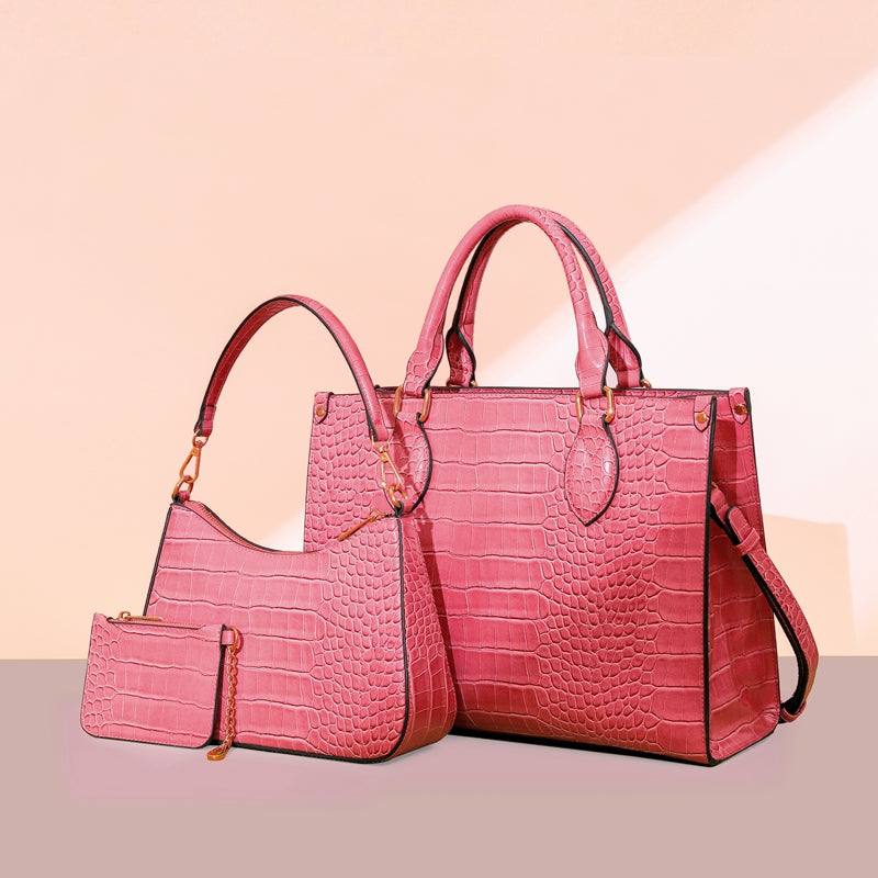 Pink crocodile-pattern PU top-handle bag, curved shoulder bag and small zip pouch with gold-tone hardware.