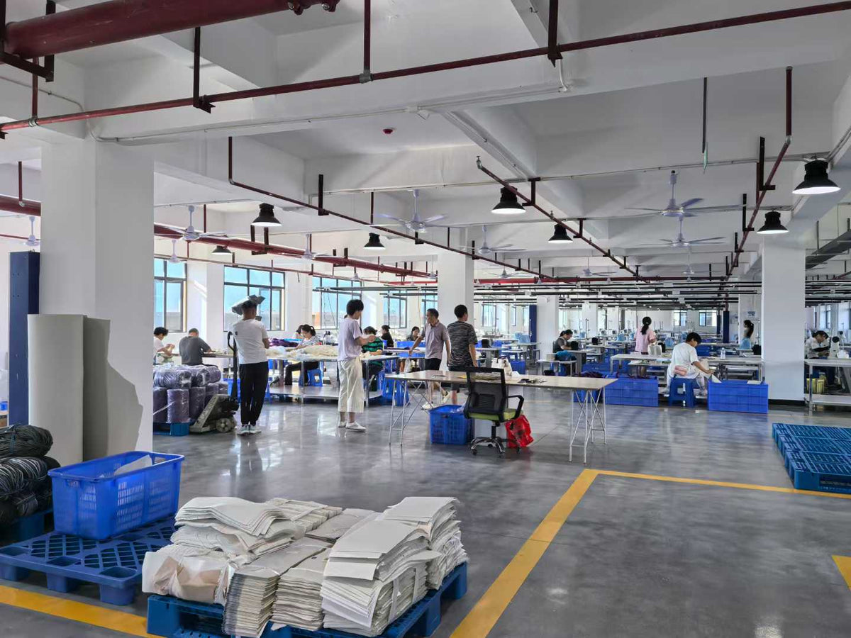 Workers preparing components beside stacks of white cut pieces and blue material bins.