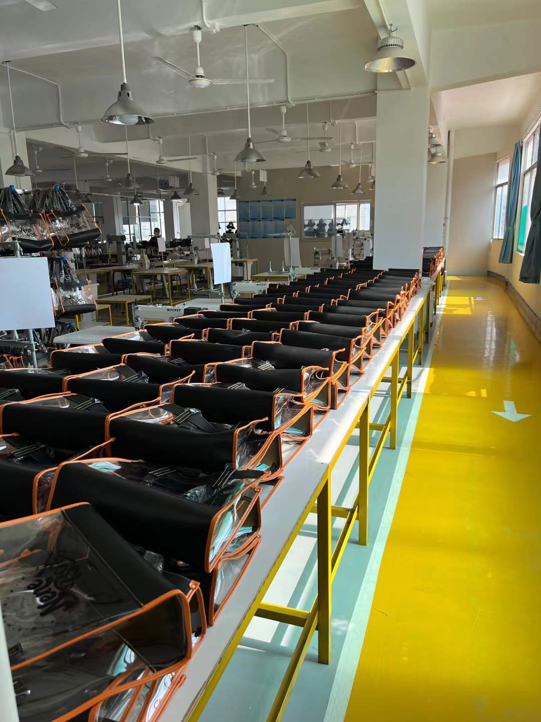 Rows of black and clear bag components with orange trim arranged on a production table.