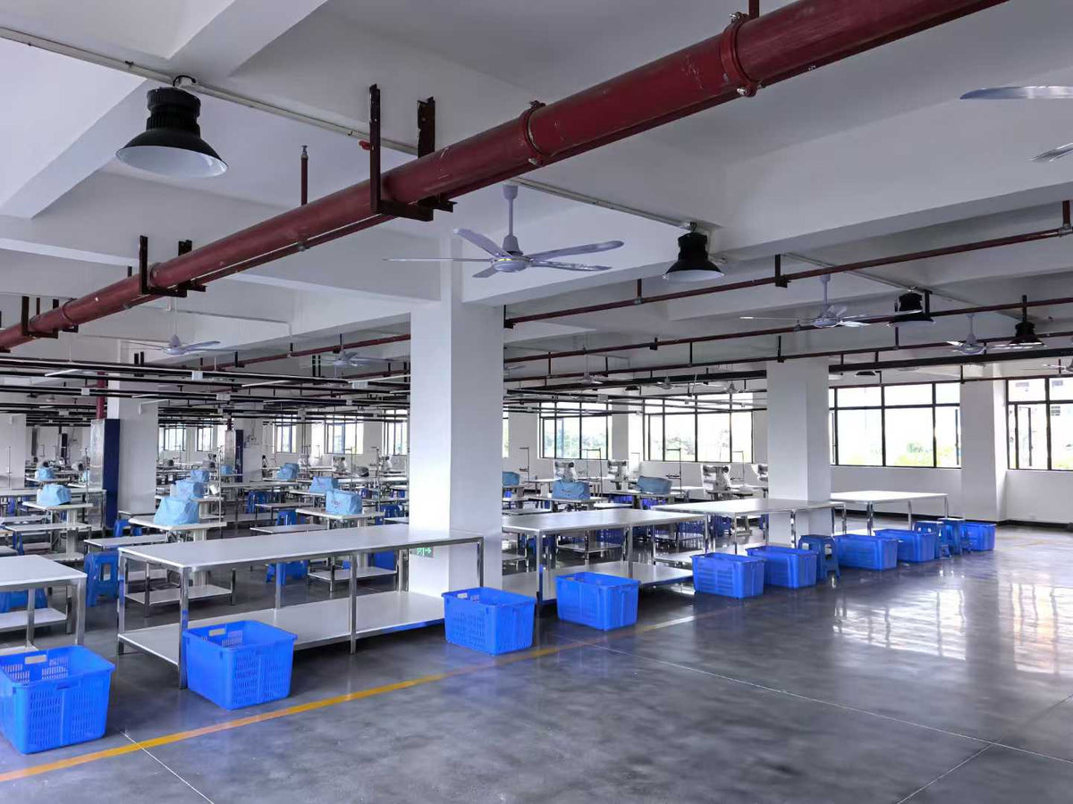 Wide view of sewing equipment and blue component bins across the factory floor.
