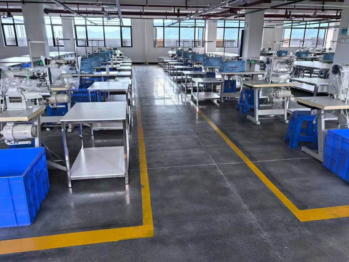Central aisle between rows of sewing machines, component tables and blue baskets.