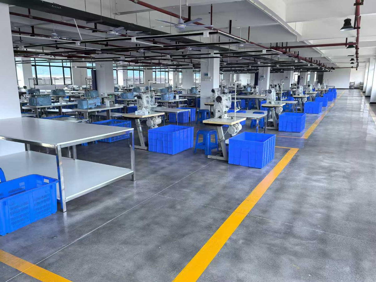 Rows of industrial sewing machines and blue component bins beside a yellow aisle line.