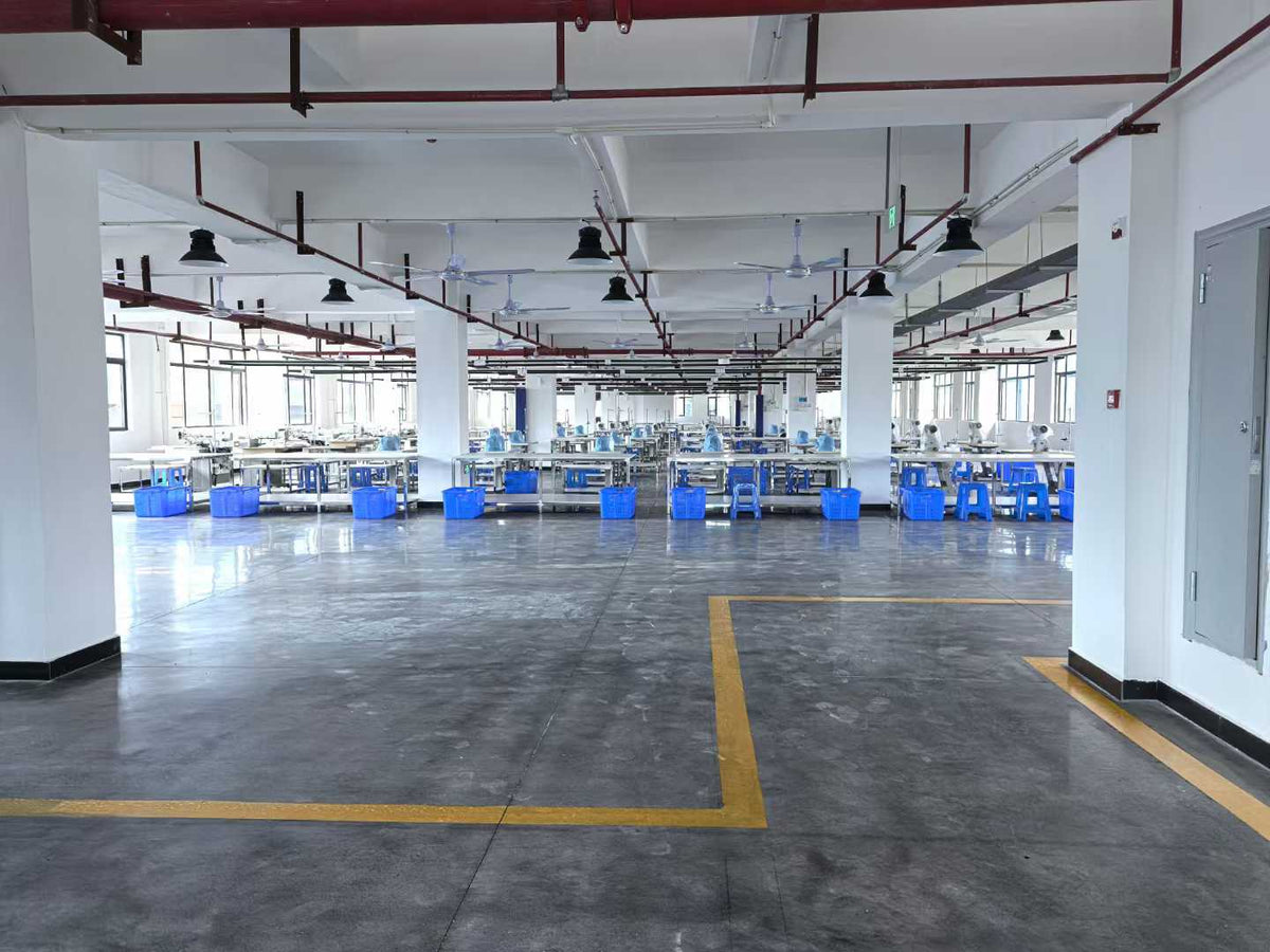 View from the entrance across sewing stations, blue baskets and a marked workshop floor.