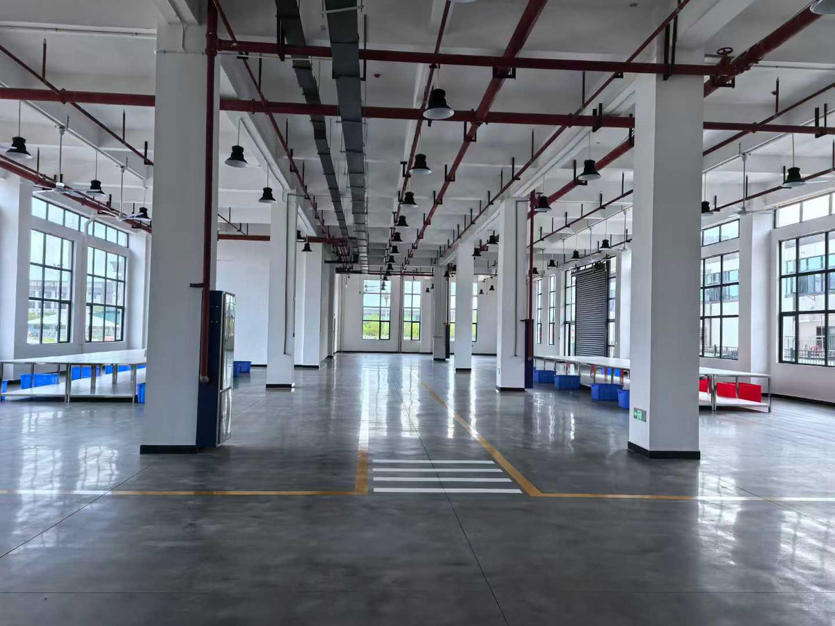 Marked factory walkway between white columns, preparation tables and component bins.