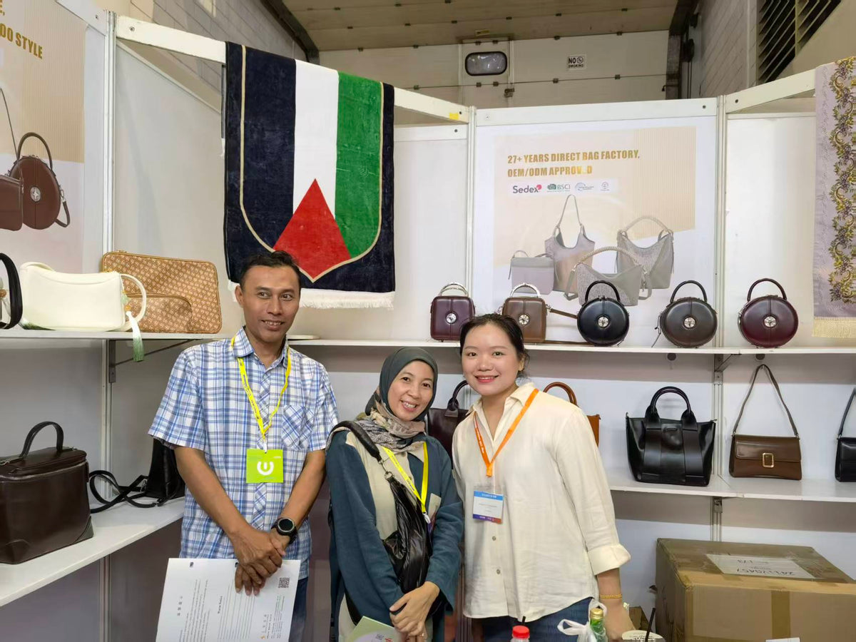 Three people posing in front of round and rectangular handbags at an exhibition booth.