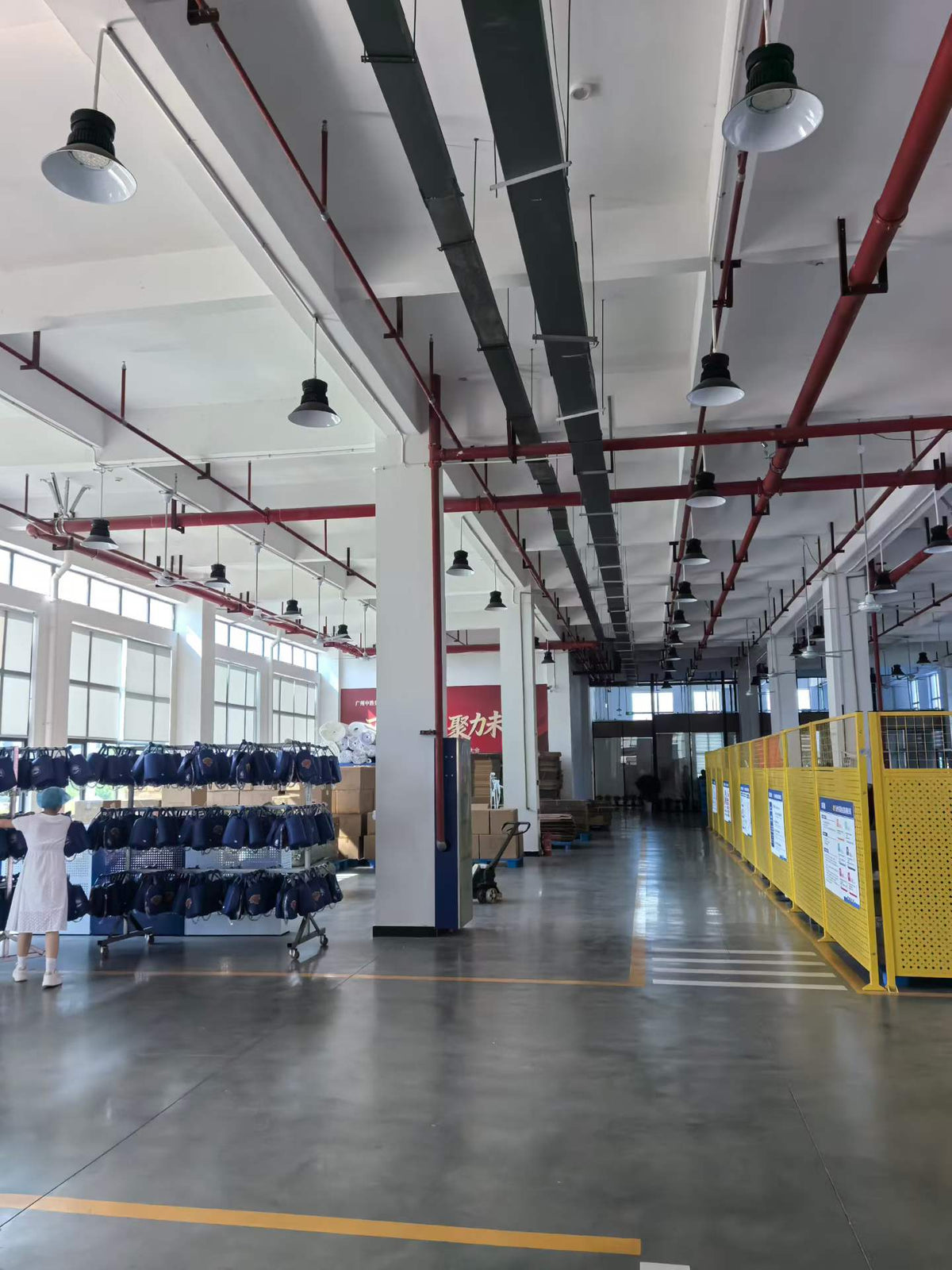 Racks of blue handbags beside a marked factory aisle and partitioned work areas.