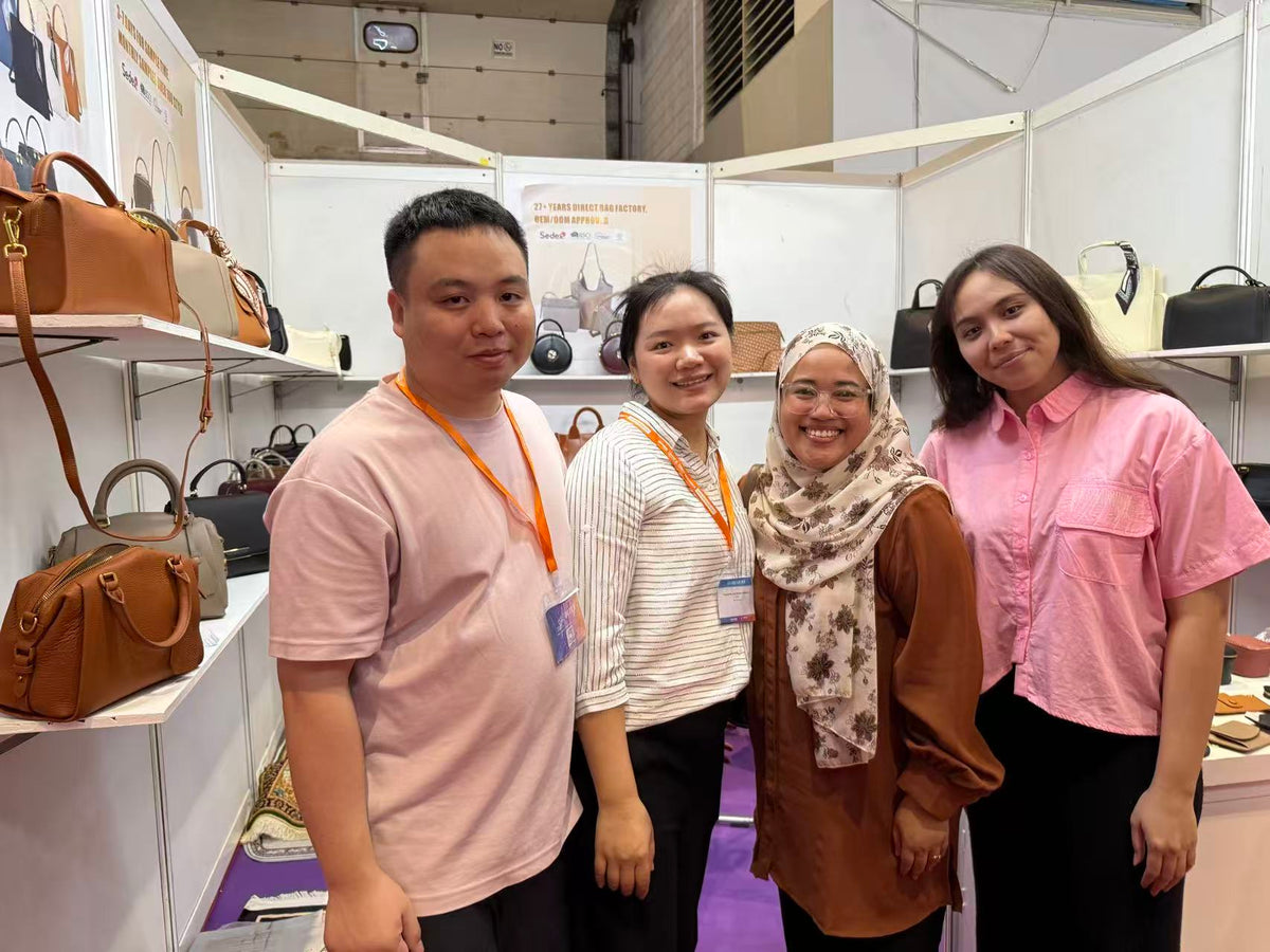 Four people posing beside shelves of handbags inside an exhibition booth.