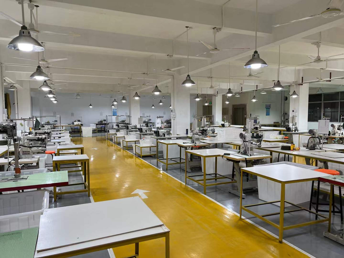 Rows of industrial sewing machines, worktables and white bins in the handbag workshop.