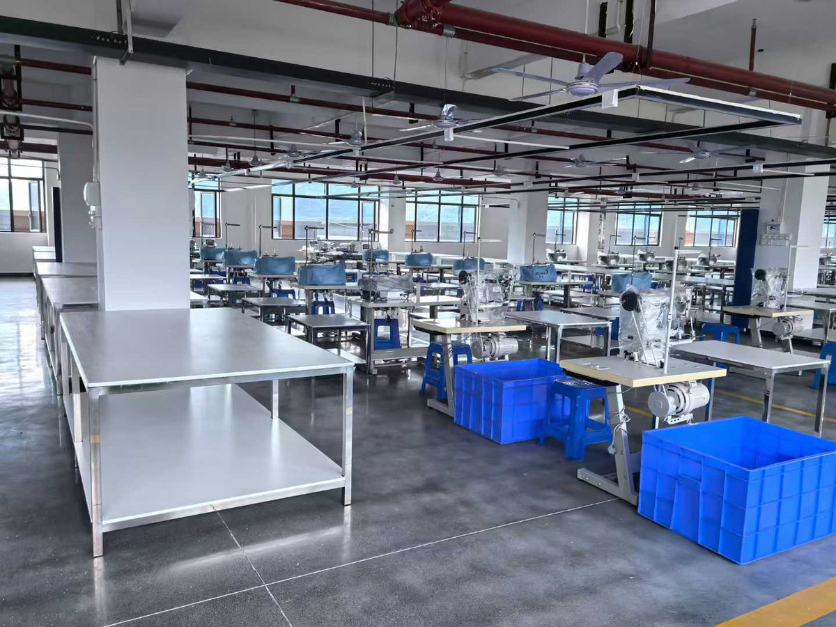 Industrial sewing equipment, preparation tables and blue bins arranged in workshop rows.