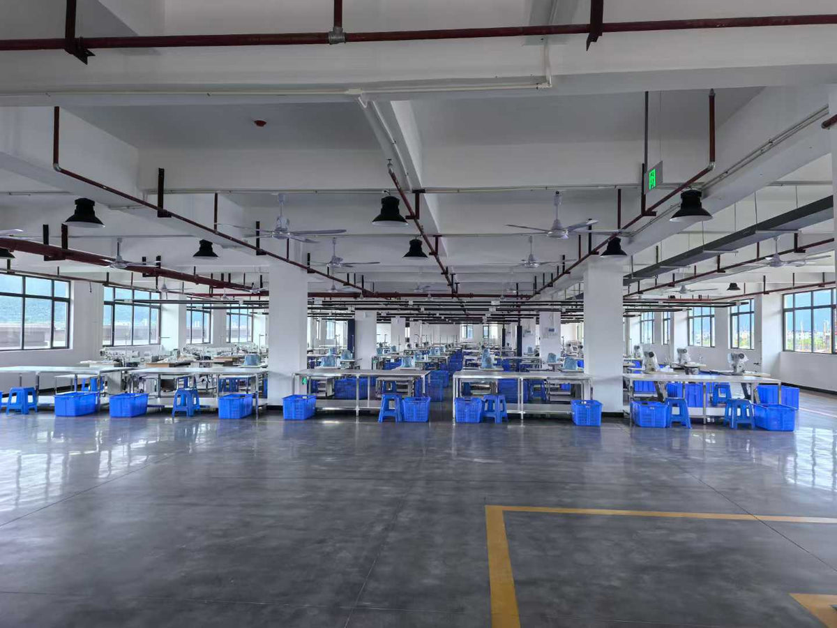 Wide factory view showing sewing stations, blue baskets and marked floor routes.