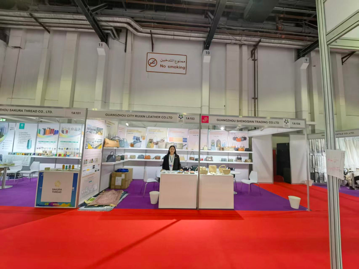 Wide view of handbag exhibition stands beside a red carpet aisle.