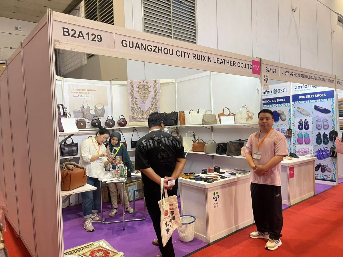 Visitors gathered around a table inside a handbag exhibition booth.