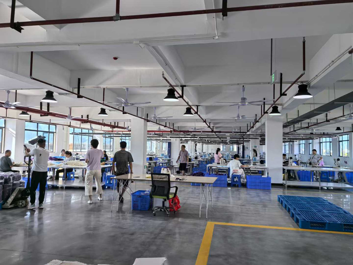 Workers handling materials at assembly tables across the bag workshop.