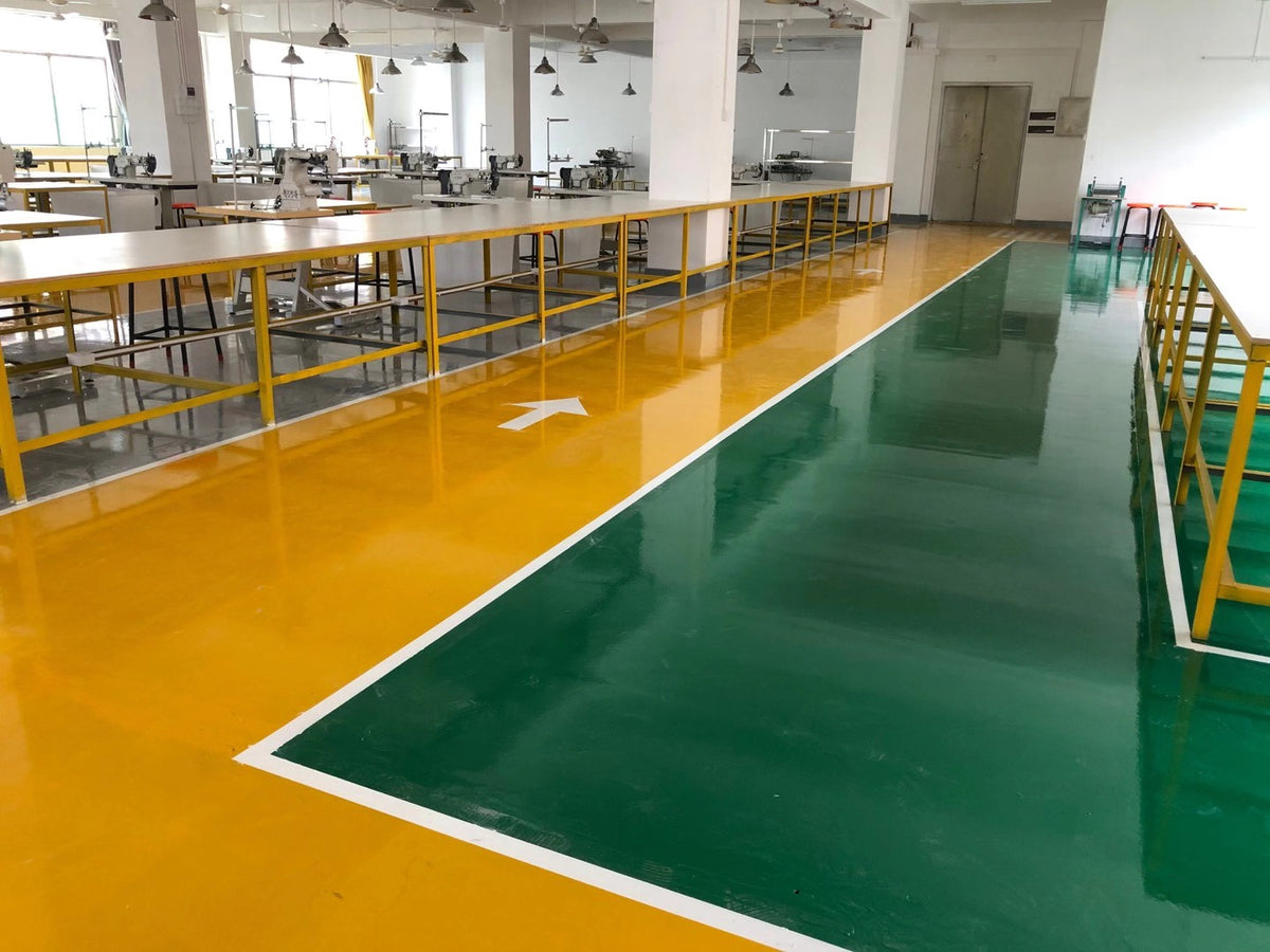 Rows of sewing machines and worktables beside marked yellow and green factory walkways.