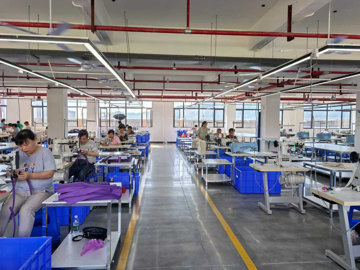 Workers handling purple bag straps and components at industrial sewing machines.
