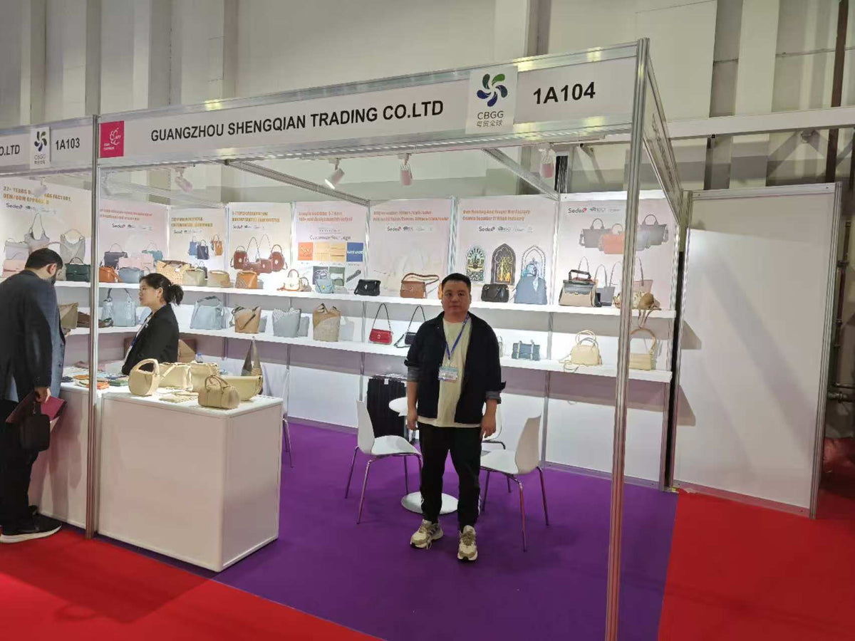A person standing in front of handbag samples and meeting tables at an exhibition booth.