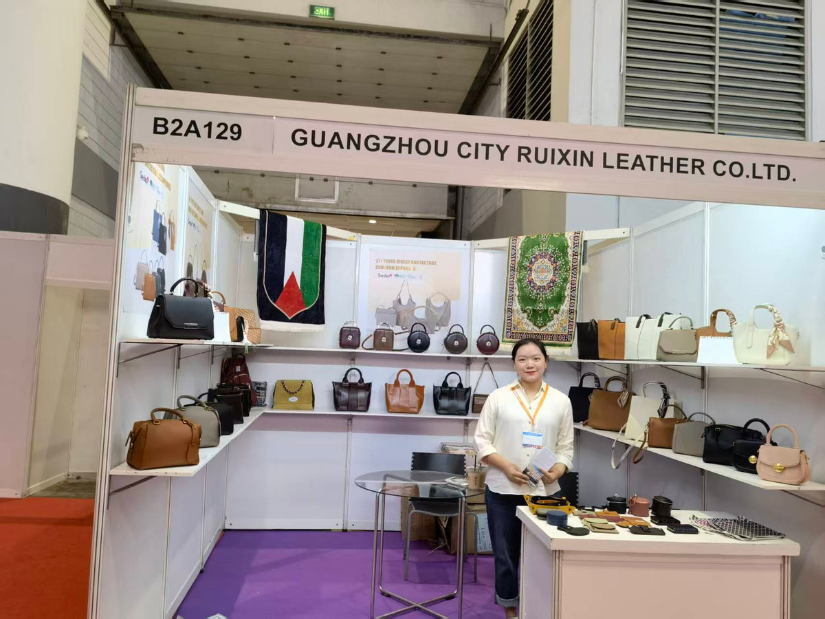 A person standing behind an accessory counter surrounded by handbags at an exhibition booth.