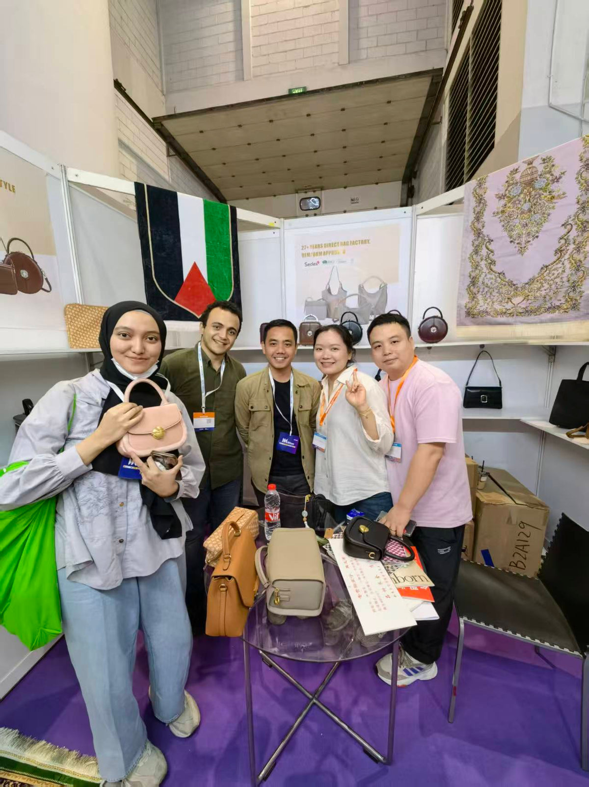 Five people posing beside a table with pink, tan and black handbag samples.