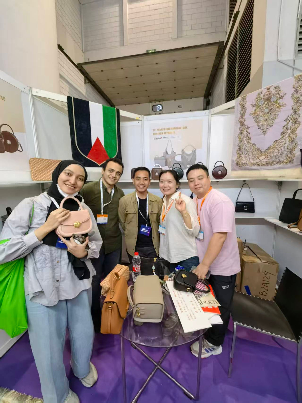 Five people posing with a pink handbag beside a table of bag samples.