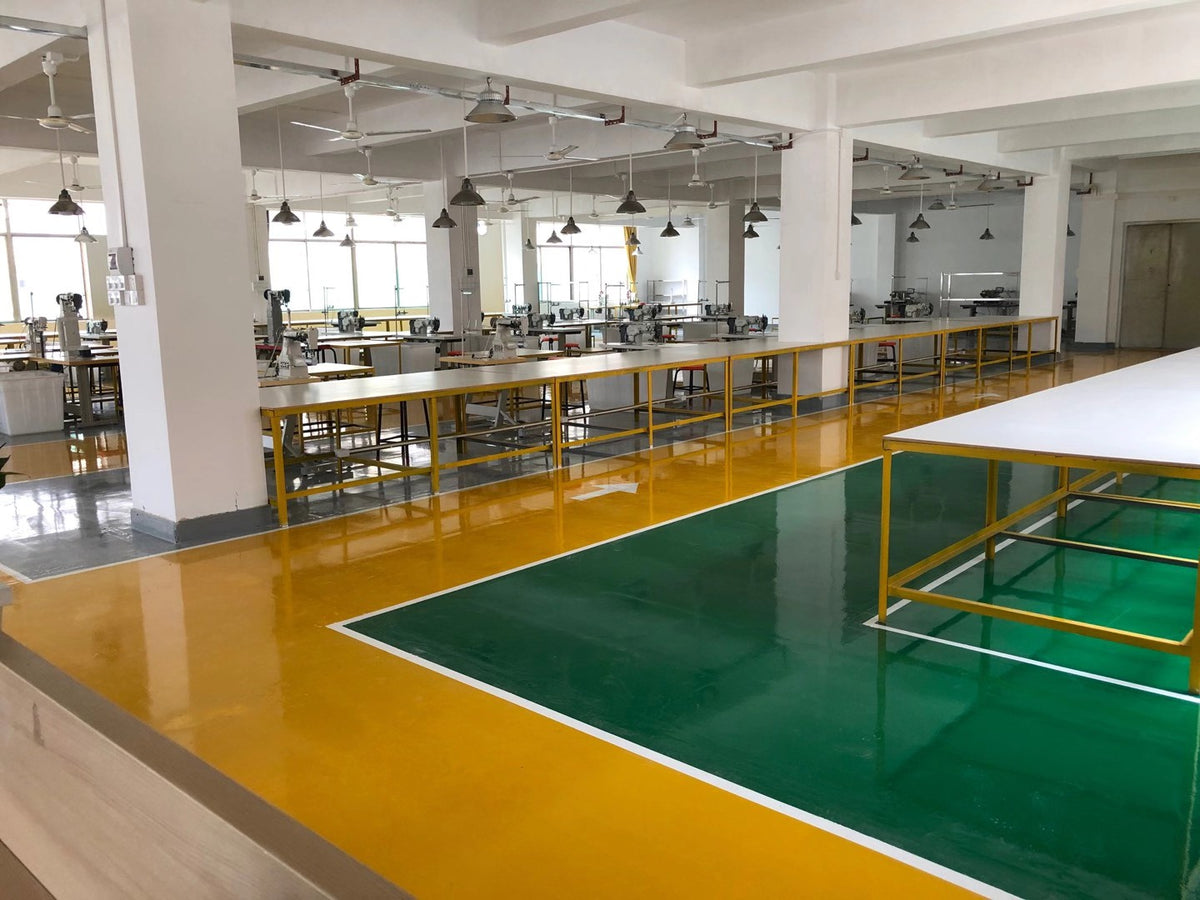 Wide view of sewing workstations, white columns and marked walkways in a bag workshop.