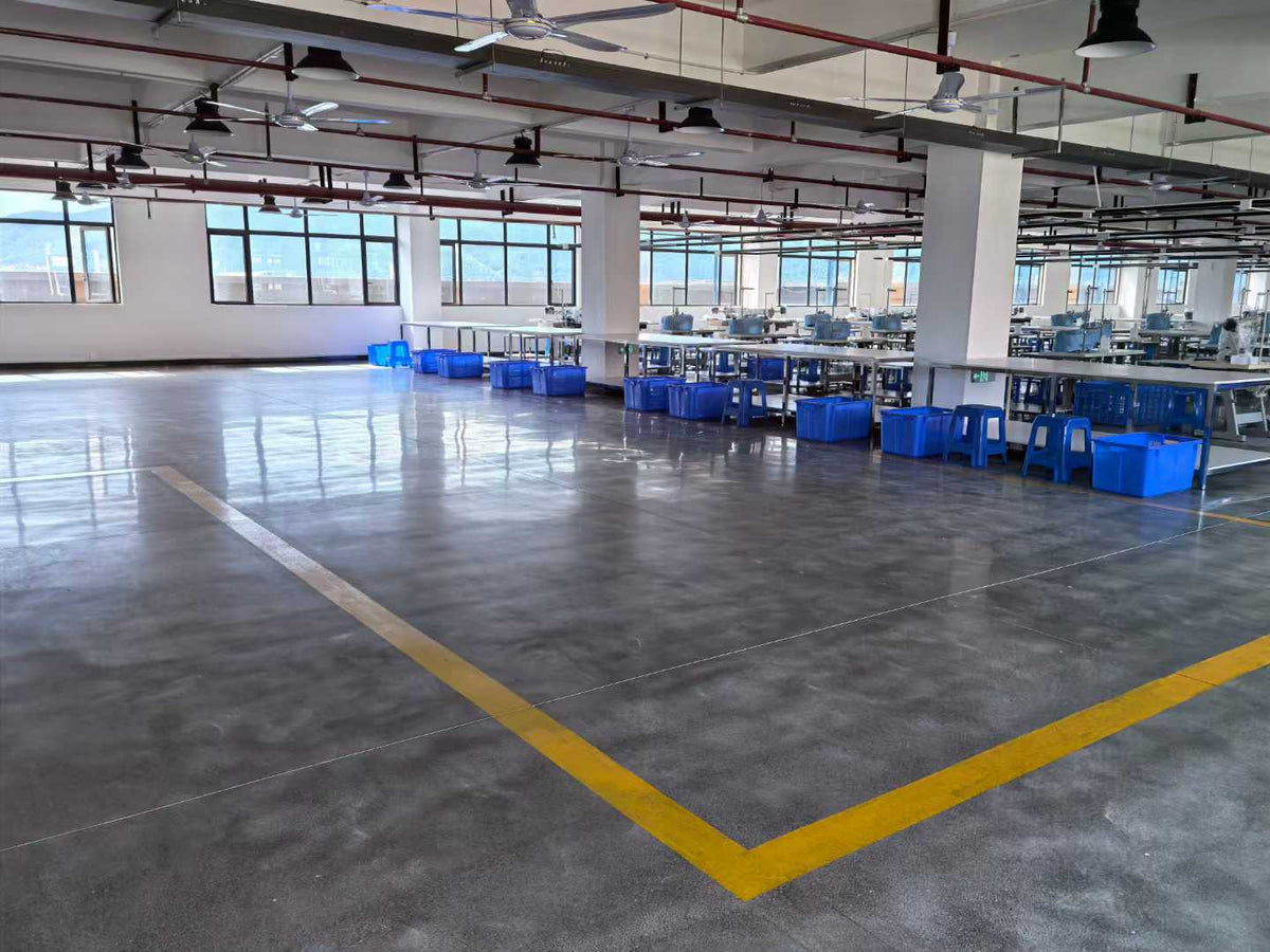 Open workshop floor beside rows of sewing tables and blue component baskets.