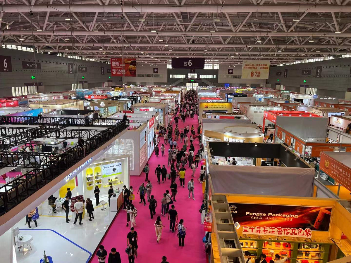 Overhead view of exhibition booths and visitors along a central trade show aisle.